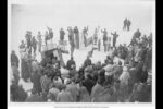 Black and white photo of a crowd of people watching a circle of men holding flags for an Olympic ceremony.