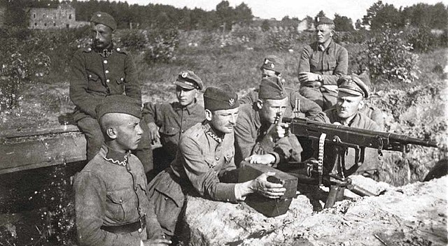 Eight men standing behind a machine gun. The men are in a trench line waiting for the soviet advance.