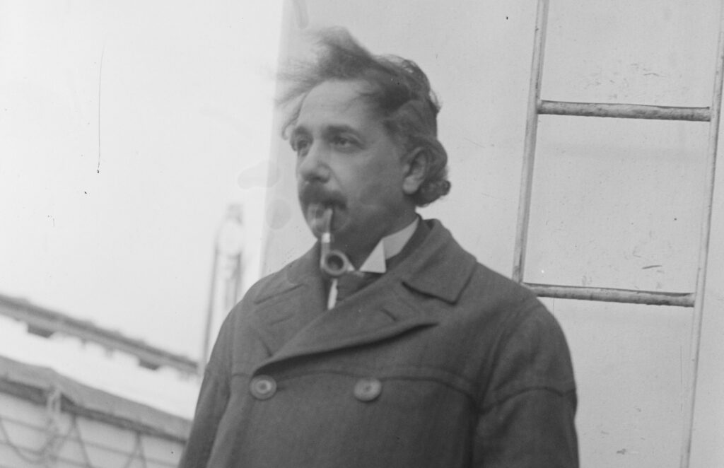 A man stands with a pipe in his mouth, looking off into the distance.