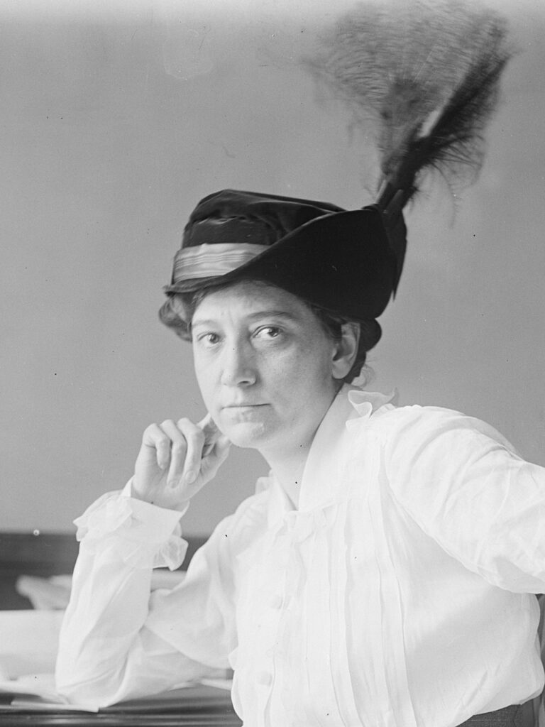 This black and white photo shows Ruth McCormick posing for a portrait. She sports a white blouse and a hat with feathers.