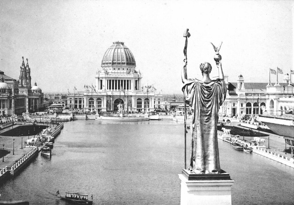 This black and white images demonstrates the center of the 1893 Columbian Exposition. The pool at the center is surrounded by white plastered buildings and the entire plaza is overlooked by a golden statue. 