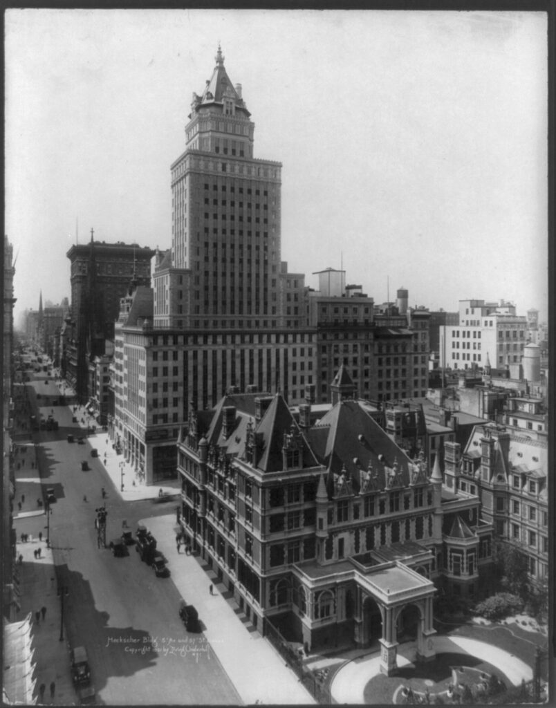 The photo is showing the New York Skyline from the perspective of someone in a building. The Heckscher building is being display as the only building that is not small or being look down upon. The roads is not busy and everything looks clean.